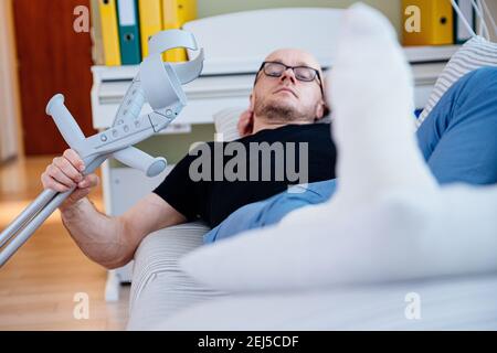 Der Mann mit der Brille liegt zu Hause mit dem Bein in Gips auf dem Sofa. Stockfoto