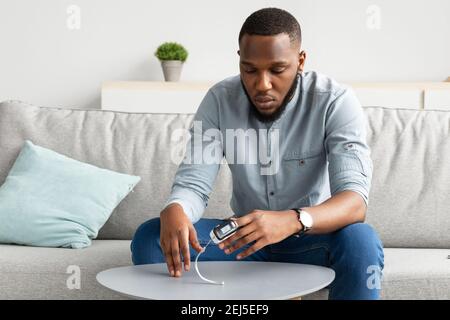 African Guy Mit Pulsoximeter Messung Der Sauerstoffsättigung In Innenräumen Stockfoto