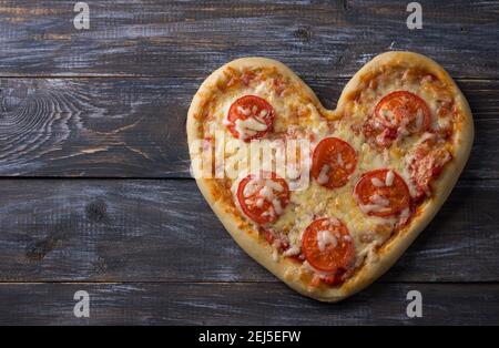 Hausgemachte leckere margarita Pizza mit Tomaten in Form eines Herzens auf einem Holztisch zum Valentinstag, Draufsicht, Platz Stockfoto