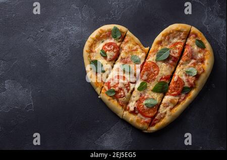 Hausgemachte leckere margarita Pizza mit Tomaten in Form eines Herzens auf schwarzem texturierten Hintergrund für Valentinstag, Draufsicht, Raum Stockfoto