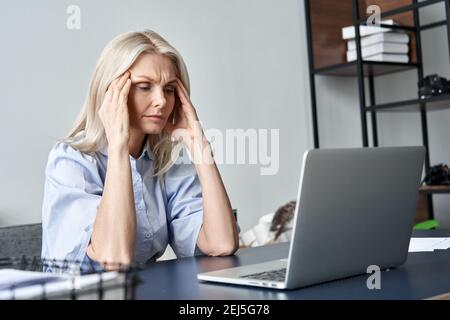 Gestresste alte Geschäftsfrau, die nach der Computerarbeit unter Kopfschmerzen leidet. Stockfoto