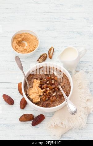 Köstliche Haferflocken in einer weißen Schüssel, Datteln Früchte, Kakao und vegane Milch. Gesundes Frühstück auf hellblauem Hintergrund. Draufsicht. Stockfoto
