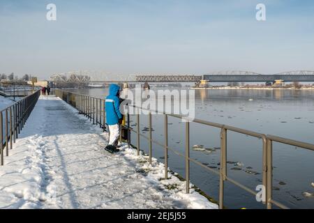 Tczew, Polen - 21. Februar 2021: Menschen auf dem Pier über der Weichsel. Die historische Brücke im Hintergrund Stockfoto