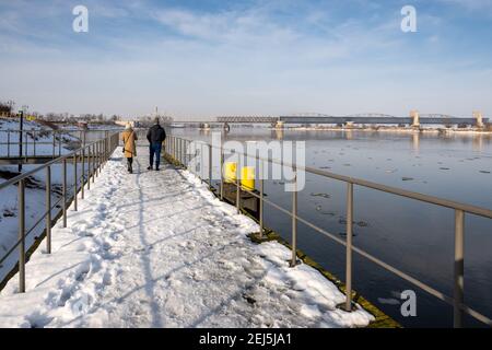 Tczew, Polen - 21. Februar 2021: Menschen auf dem Pier über der Weichsel. Die historische Brücke im Hintergrund Stockfoto