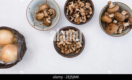 Frische rohe braune Pilze in einer Schüssel und gelbe Zwiebel im Korb, Nahaufnahme von oben mit Kopierplatz. Stockfoto