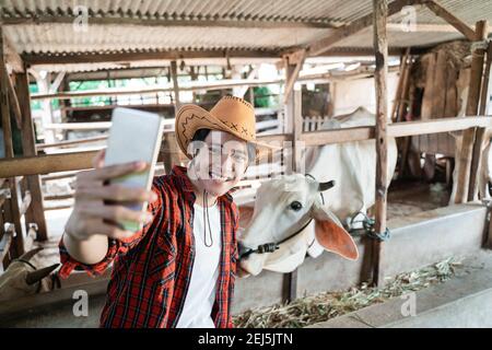 Mann trägt Cowboy Hut Selfie mit Handtelefon in Kuhfarm Hintergrund Stockfoto