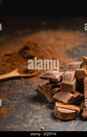 Verschiedene Stücke von dunkler Schokolade und Kakaopulver auf dunkler Oberfläche. Stockfoto