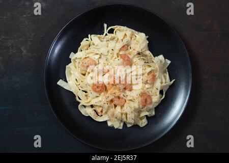 Köstliche italienische Pasta. Fetuccini mit Garnelen und Kräutersauce auf schwarzem Teller. Stockfoto