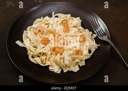 Köstliche italienische Pasta. Fetuccini mit Garnelen und Kräutersauce auf schwarzem Teller. Stockfoto