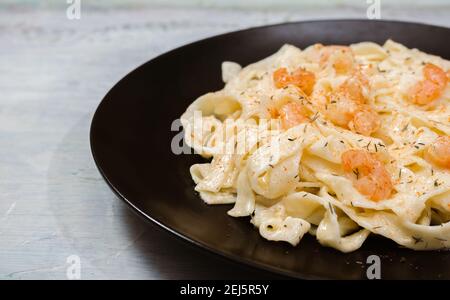 Köstliche italienische Pasta. Fetuccini mit Garnelen und Kräutersauce auf schwarzem Teller. Stockfoto