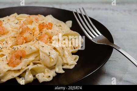 Köstliche italienische Pasta. Fetuccini mit Garnelen und Kräutersauce auf schwarzem Teller. Stockfoto