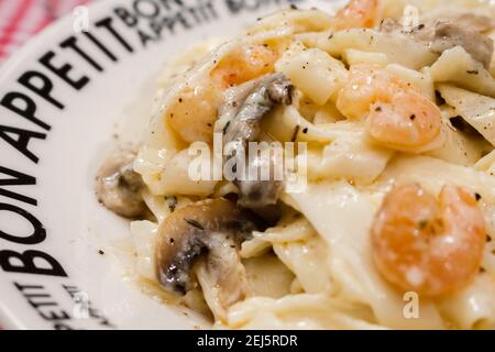 Köstliche Fettuccine mit Sahne Sauce von Pilzen und Garnelen auf einem Teller, der Bon Appetit mit rot karierten Tischdecke sagt. Italienische Küche. Stockfoto