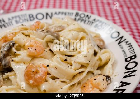 Köstliche Fettuccine mit Sahne Sauce von Pilzen und Garnelen auf einem Teller, der Bon Appetit mit rot karierten Tischdecke sagt. Italienische Küche. Stockfoto