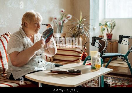 Ältere Schönheit und Hautpflege. Ältere ältere Menschen plus Größe blonde Frau mit Behinderung Anwendung schwarze Mascara in der Nähe des Spiegels zu Hause. Stockfoto