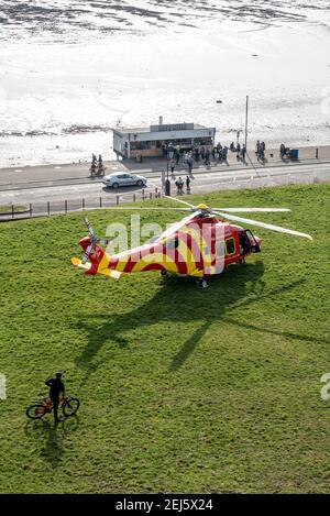 Essex & Herts Air Ambulance landete an einem sonnigen Wintertag auf Klippen in Southend on Sea, Essex, Großbritannien, während der COVID 19-Sperre. Fahrradfahrer beobachten Stockfoto