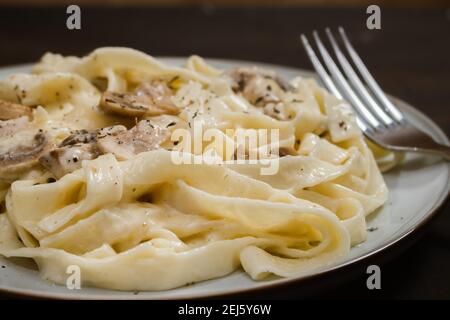 Ausgefallene Bio-Fetuccine-Pasta mit cremiger alfredo-Pilzsauce. Rustikale Platte und dunkle Oberfläche. Stockfoto