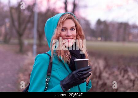 Junge Rotschopf Frau hält Tasse heißen Drink bei kaltem Wetter, türkisfarbene Kapuzenmantel Stockfoto