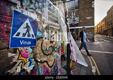 GROSSBRITANNIEN / England / London / EIN Mann mit Gesichtsmaske kommt an der Covid-19 Street Art vorbei, in der Nähe der Brick Lane in London. Stockfoto