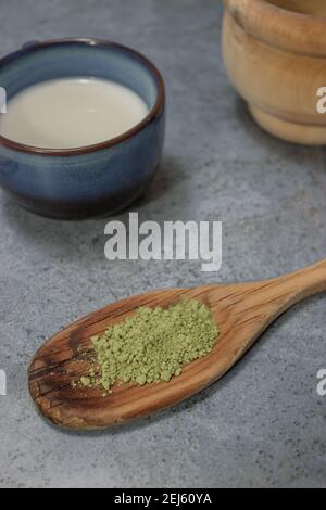 Draufsicht vertikal gesundes Matcha-Teepulver auf Holzlöffel mit einer Tasse Milch und Zucker in einem Grauen Stein Hintergrund. Japanischer Grüner Tee Konzept. Stockfoto
