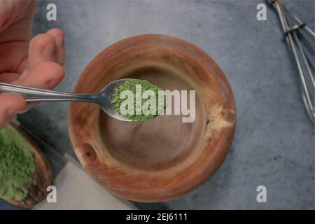 Vertikales Bild Matcha-Tee-Pulver Gießen in Holzschale auf Graustein Hintergrund. Japanischer Grüner Tee Konzept. Matcha Tee Zubereitung Zutat 2021. Stockfoto
