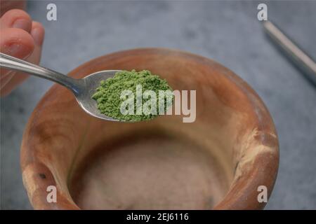 Vertikales Bild Matcha-Tee-Pulver Gießen in Holzschale auf Graustein Hintergrund. Japanischer Grüner Tee Konzept. Matcha Tee Zubereitung Zutat 2021. Stockfoto