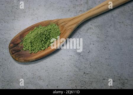 Nahaufnahme Matcha-Teepulver auf Holzlöffel auf Grey Stone Hintergrund. Japanischer Grüner Tee Konzept. Matcha Tee Zubereitung Zutat 2021. Stockfoto