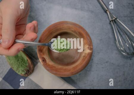 Horizontales Bild Matcha-Tee-Pulver Gießen in Holzschüssel auf Grey Stone Hintergrund. Japanische Matcha Tee Zubereitung Zutat 2021. Stockfoto