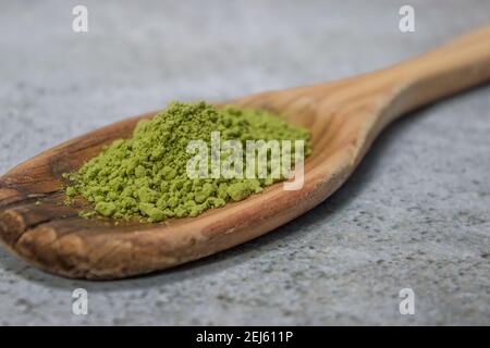 Nahaufnahme Matcha-Teepulver auf Holzlöffel auf Grey Stone Hintergrund. Japanischer Grüner Tee Konzept. Matcha Tee Zubereitung Zutat 2021. Stockfoto