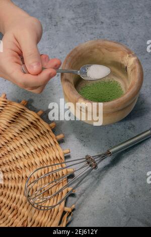 Vertikales Bild Matcha-Teepulver auf der Oberseite und Löffel mit Zucker auf kleine Tonschüssel auf Grey Stone Hintergrund gießen. Japanische Matcha Tee Zubereitung. Stockfoto