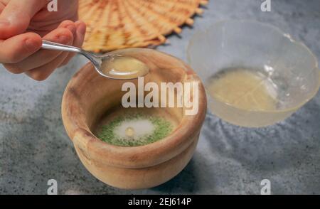 Horizontales Bild von Tonschüssel Matcha Teepulver mit Zucker beim Gießen von Honig mit einem Löffel auf Grey Stone Hintergrund. Japanische Matcha Tee Zubereitung. Stockfoto