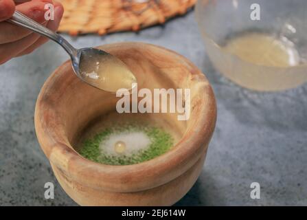 Horizontales Bild von Tonschüssel Matcha Teepulver mit Zucker beim Gießen von Honig mit einem Löffel auf Grey Stone Hintergrund. Japanische Matcha Tee Zubereitung. Stockfoto