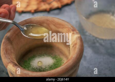 Horizontales Bild von Tonschüssel Matcha Teepulver mit Zucker beim Gießen von Honig mit einem Löffel auf Grey Stone Hintergrund. Japanische Matcha Tee Zubereitung. Stockfoto