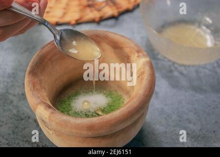 Horizontales Bild von Tonschüssel Matcha Teepulver mit Zucker beim Gießen von Honig mit einem Löffel auf Grey Stone Hintergrund. Japanischer Matcha Tee 2021. Stockfoto