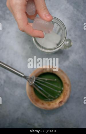 Vertikales Bild von Tonschale Matcha Tee neben einem Kristallglas mit Eis auf Grey Stone Hintergrund. Japanische Matcha Tee Zubereitung 2021. Stockfoto