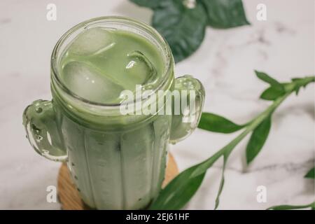 Horizontales Bild Iced Matcha Tee auf weißem Marmor Hintergrund mit einigen Pflanzen. Zubereitung Von Matcha-Tee 2021. Stockfoto