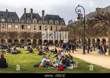 Paris, Frankreich - 21. Februar 2021: Menschen entspannen auf grünen Rasen des berühmten Place des Vosges - älteste geplante Platz in Paris, während covid-19 pandemi Stockfoto