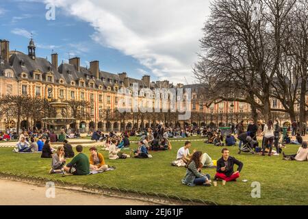 Paris, Frankreich - 21. Februar 2021: Menschen entspannen auf grünen Rasen des berühmten Place des Vosges - älteste geplante Platz in Paris, während covid-19 pandemi Stockfoto