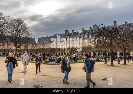 Paris, Frankreich - 21. Februar 2021: Menschen entspannen auf grünen Rasen des berühmten Place des Vosges - älteste geplante Platz in Paris, während covid-19 pandemi Stockfoto