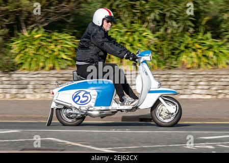 Lambretta Motorroller wird von einem weißen Mann mittleren Alters in Southend on Sea, Essex, Großbritannien, an einem hellen sonnigen Wintertag gefahren, während COVID 19 Lockdown Stockfoto