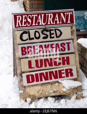 Ein altes, verschneite Schild vor einem geschlossenen Restaurant, ein Zeichen für die deprimierte Wirtschaft aufgrund der COVID-19 Pandemie. Stockfoto