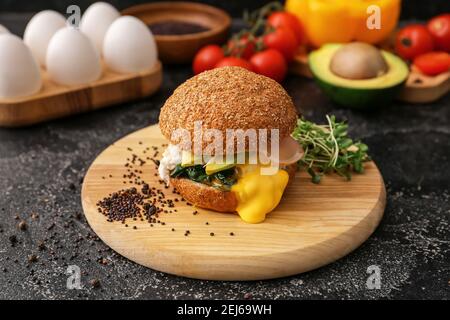 Leckerer Burger mit florentiner Ei und frischem Gemüse auf dunklem Hintergrund, Nahaufnahme Stockfoto