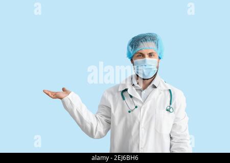 Arzt in medizinischer Maske zeigt etwas auf farbigem Hintergrund Stockfoto