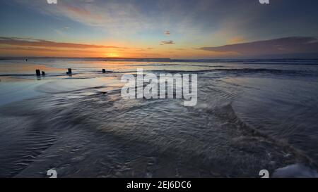 Tramore Beach, Waterford, Irland. Lange Exposition von Wellen am Strand mit irischen Momunento im Hintergrund. Kräftiger Sonnenaufgang. Stockfoto