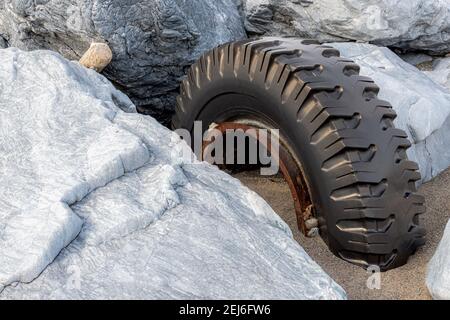 Ein großer, abgenutzter LKW-Reifen, der halb im Sand zwischen großen Kalksteinfelsen vergraben ist. Reifen ist auf einer rostigen Metallfelge. Stockfoto