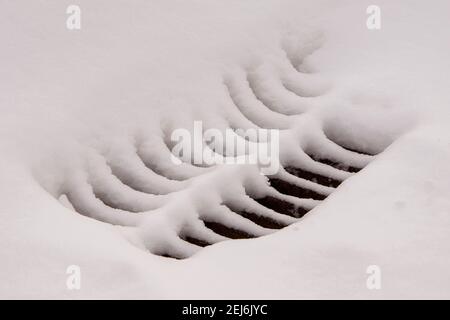 Das Gitter des Sturmabwasserkanals ist mit Schnee bedeckt Stockfoto