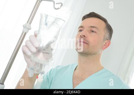 Porträt eines Krankenpflegers, der einen Perfusionsbeutel justiert Stockfoto