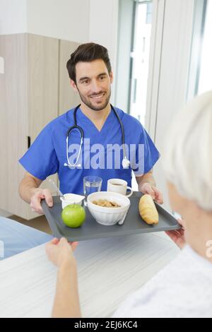 Männliche Krankenschwester, die in der Klinik Essen für ältere weibliche Patienten serviert Stockfoto