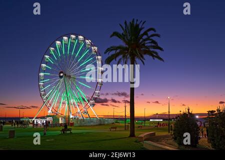 Adelaide, South Australia - 22. Februar 2021: Glenelg Mix102,3 Giant Ferris Wheel am Moseley Square beleuchtet in der Dämmerung in Richtung des Anlegeplatzes. Stockfoto