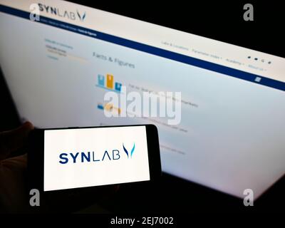 Person, die Mobiltelefon mit Logo des deutschen medizinischen Diagnostikunternehmens SYNLAB Group auf dem Bildschirm vor der Webseite hält. Fokus auf Handy-Display. Stockfoto