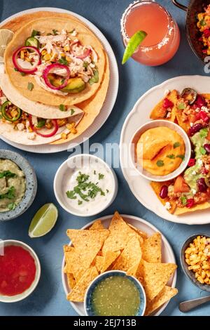 Mexikanisches Essen auf blauem Hintergrund. Nachos, Tacos und Dips, Cocktails, Overhead Shot Stockfoto